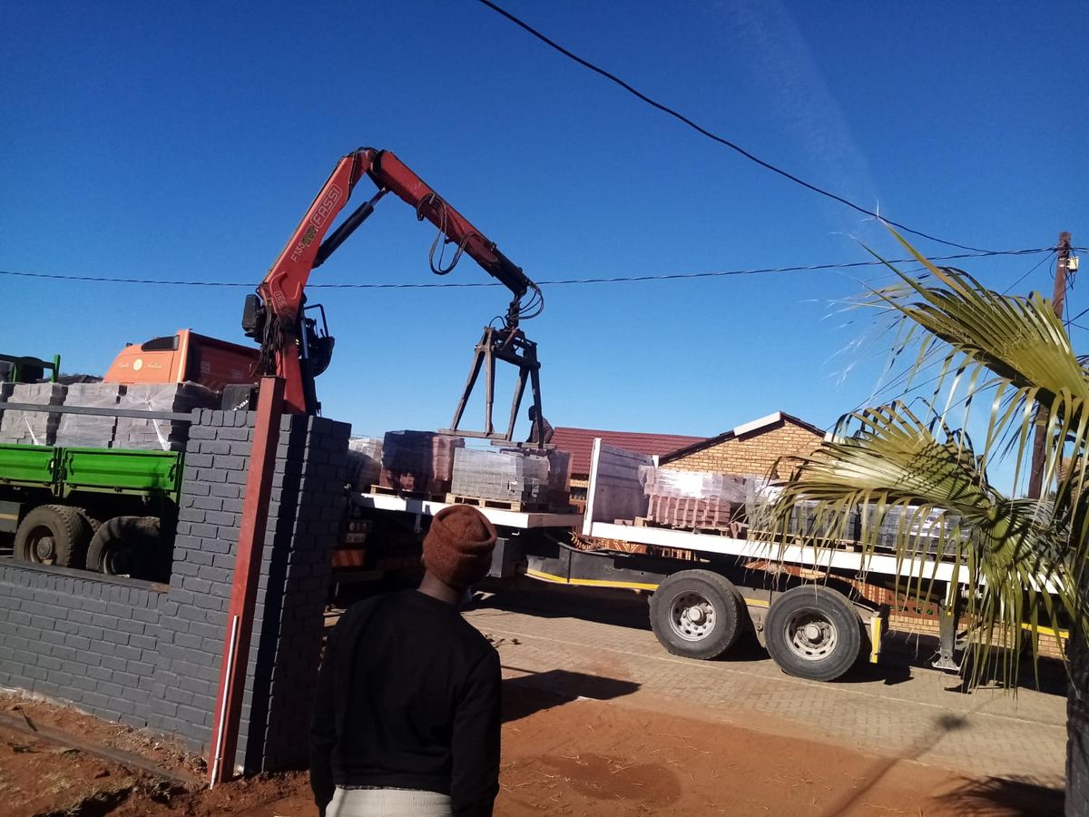 Crane truck lifting pallets of bricks into a site